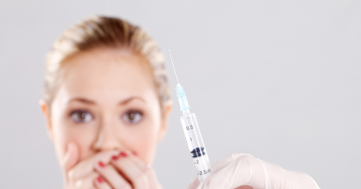 Close-up of an scared adult woman displaying a loaded syringe before administering medication.