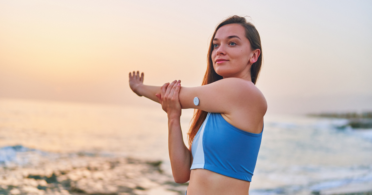 Woman with diabetes stretches her arms on a sunrise beach, demonstrating healthy lifestyle habits that support balanced blood glucose and daily energy