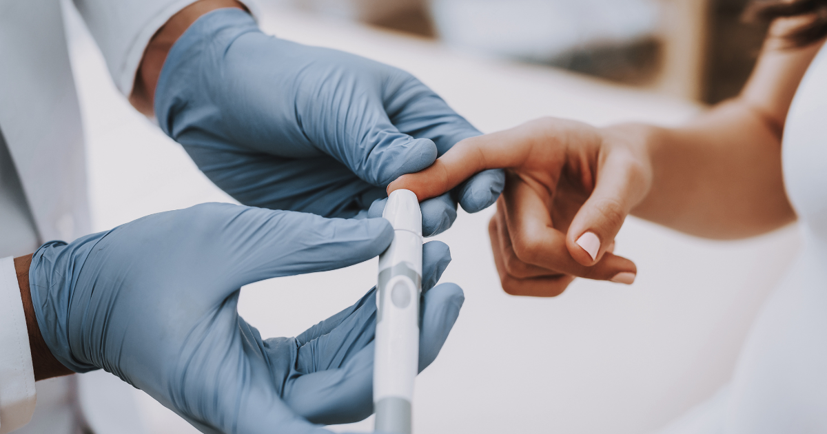 Gloved clinician presses lancet on patient’s fingertip to collect blood droplet for an accurate blood-glucose fingerstick.