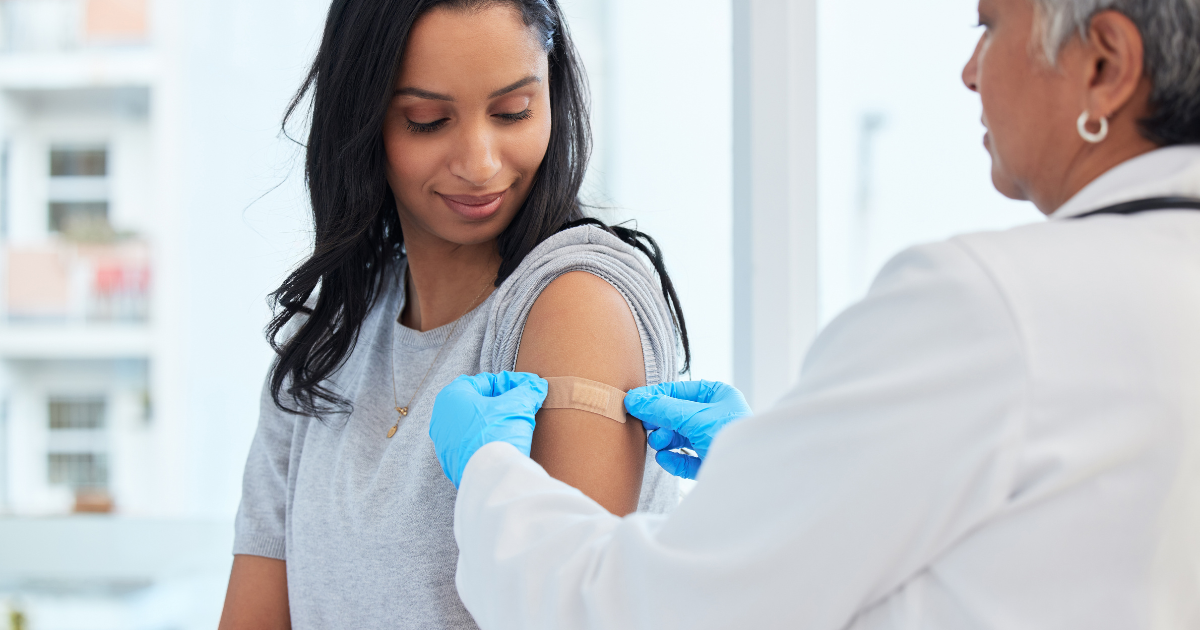 Clinician in blue gloves gives a smiling young woman an upper-arm injection in a bright clinic, demonstrating a calm, near-painless shot experience.