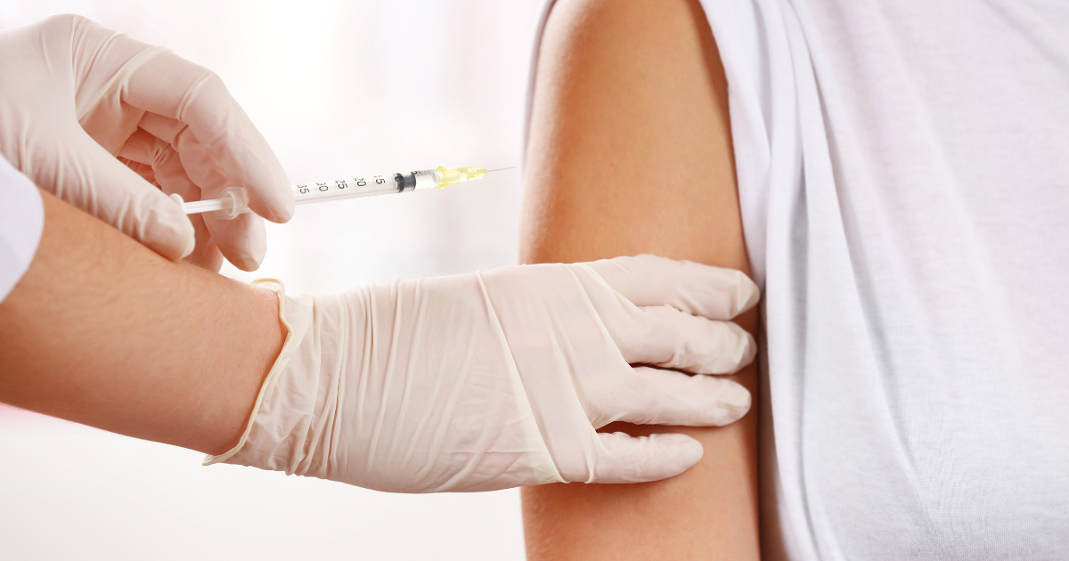 Gloved healthcare professional preparing an upper-arm injection on an adult patient