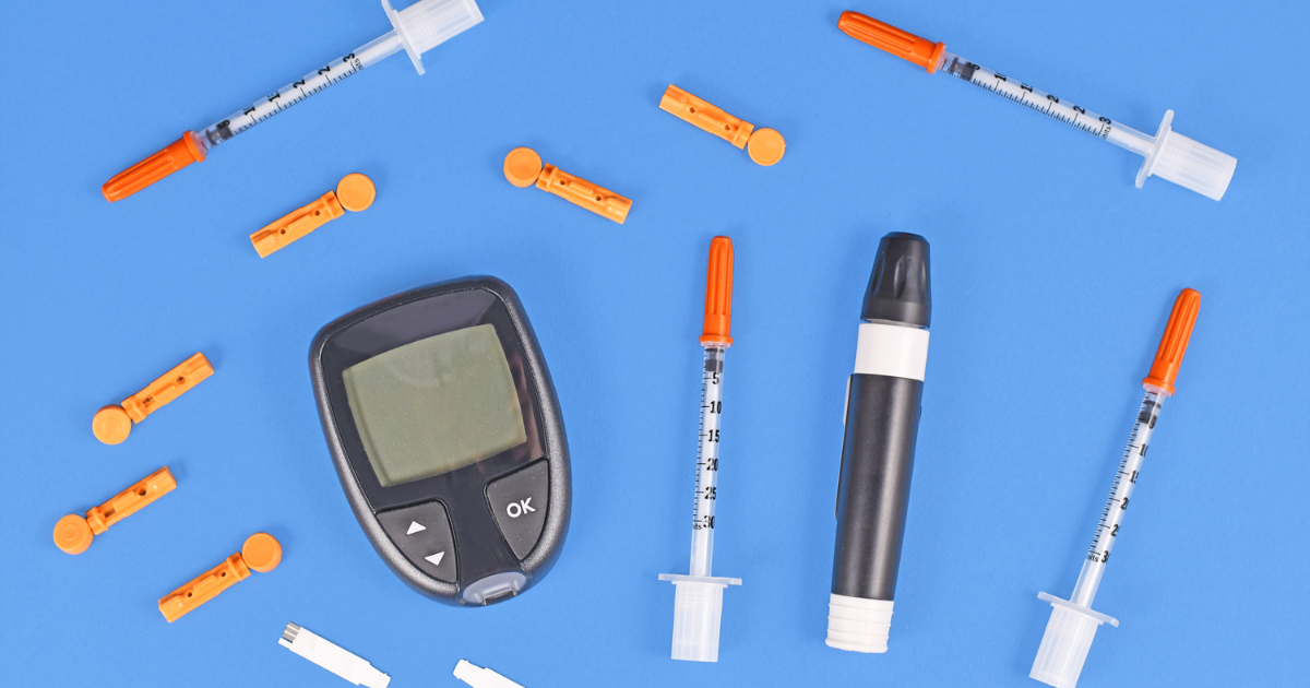 Flat-lay of glucose meter, syringes, and lancets on a blue surface, showing essential diabetes tools.